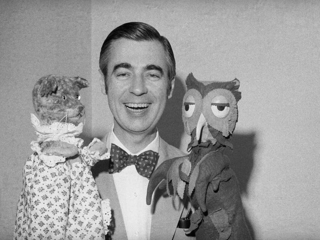 Mr. Rogers Quotes - Fred Rogers smiling while holding two puppets, one resembling a cat in a dress and the other resembling an owl with droopy eyes. The person is wearing a bow tie and a suit. The background is plain. The image is in black and white.