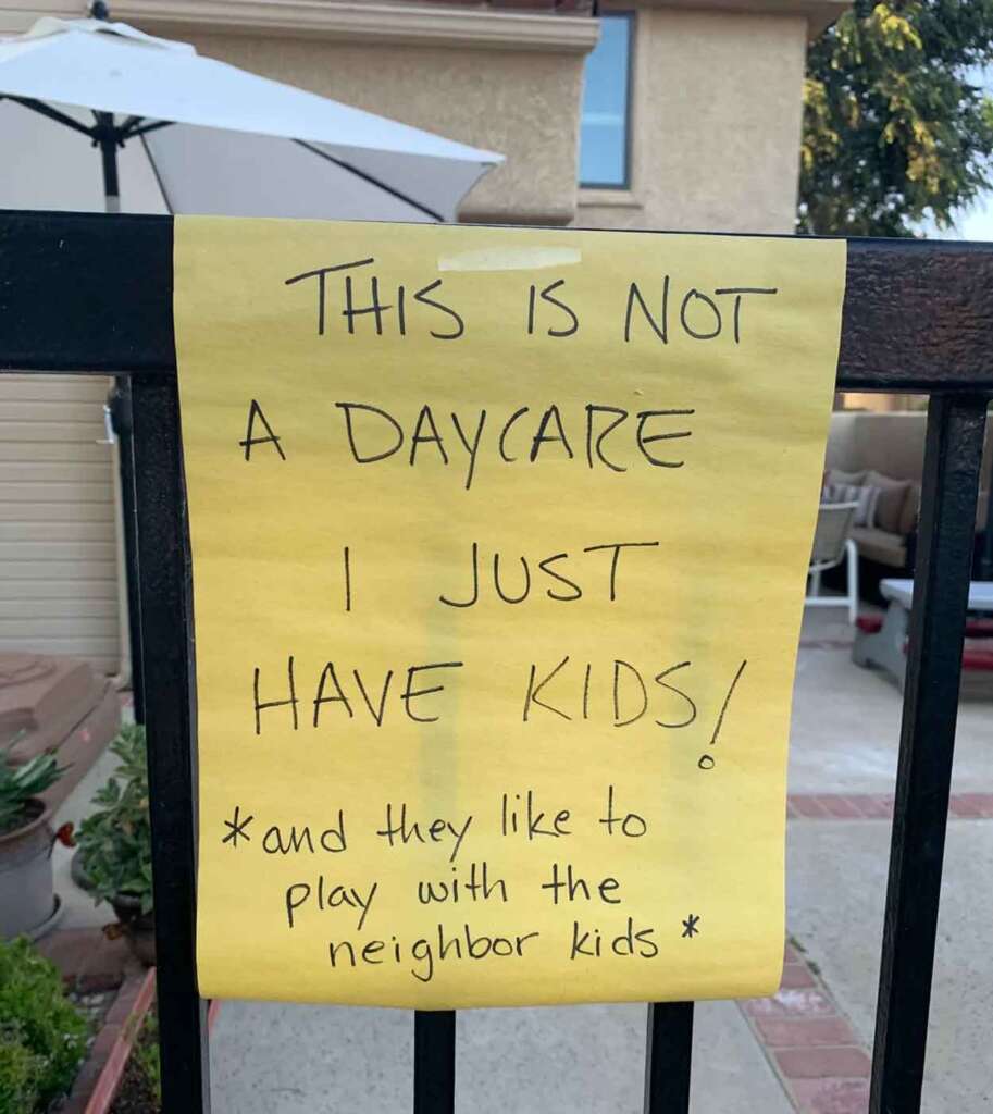 A handwritten note on a yellow paper attached to a fence reads, "This is not a daycare. I just have kids! *and they like to play with the neighbor kids*". In the background, there's a patio area with an umbrella and outdoor furniture.