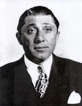 Black and white portrait of a man in a suit and tie, with slicked-back hair.