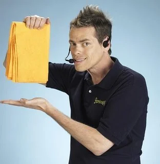 A person wearing a headset and a dark polo shirt is holding up several bright orange cloths. They are smiling and gesturing with one hand beneath the cloths as if presenting them. The background is a plain light blue.