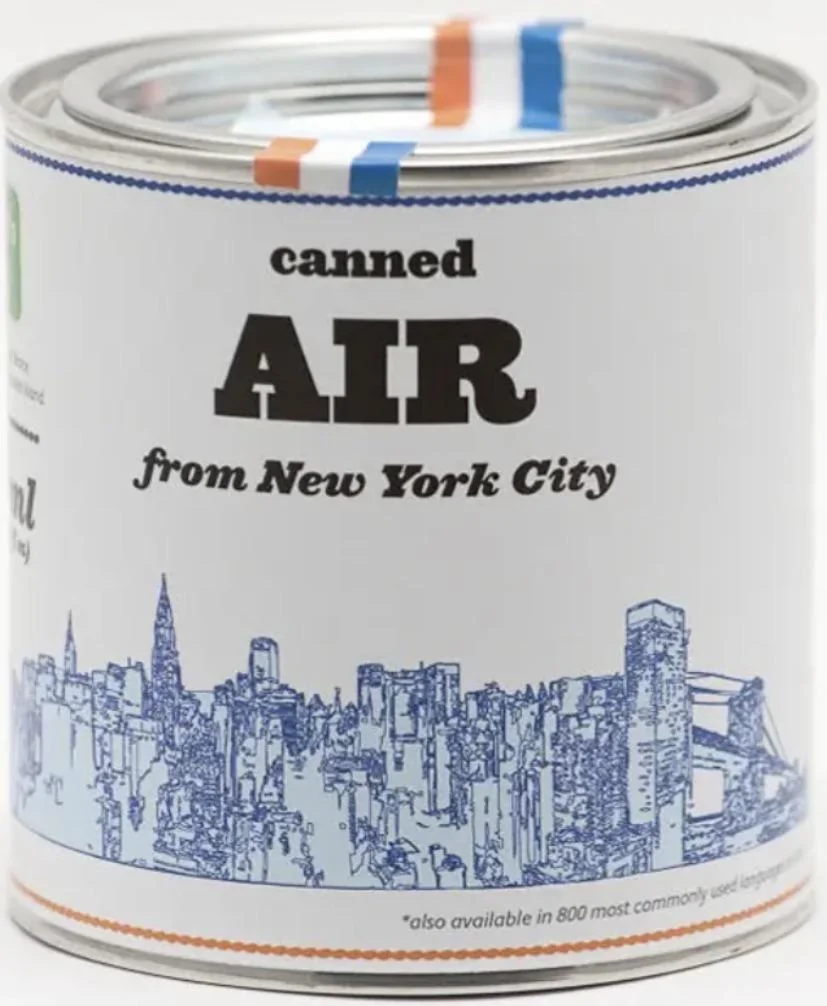 A can labeled "Canned Air from New York City" with an illustration of the New York City skyline in blue. The can features blue and orange stripes near the top and additional text at the bottom.