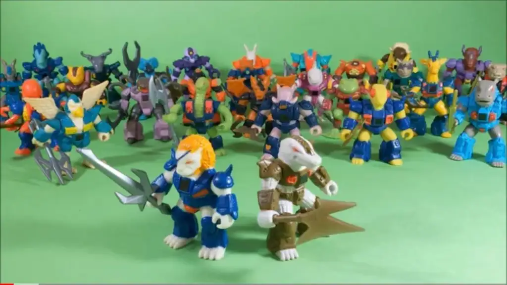 A group of colorful, small action figures with animal features standing on a green surface. In the foreground, two figures wielding weapons are prominently displayed, while a diverse array of similar figures stand grouped behind them.