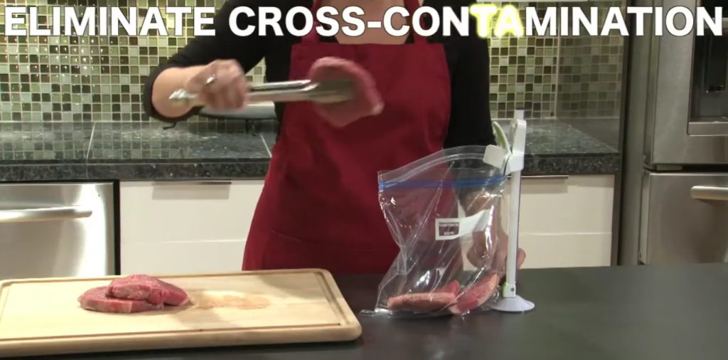 A person wearing a red apron uses tongs to place raw meat into a plastic bag on a stand. The cutting board on the counter holds more raw meat. The text above reads, "ELIMINATE CROSS-CONTAMINATION.