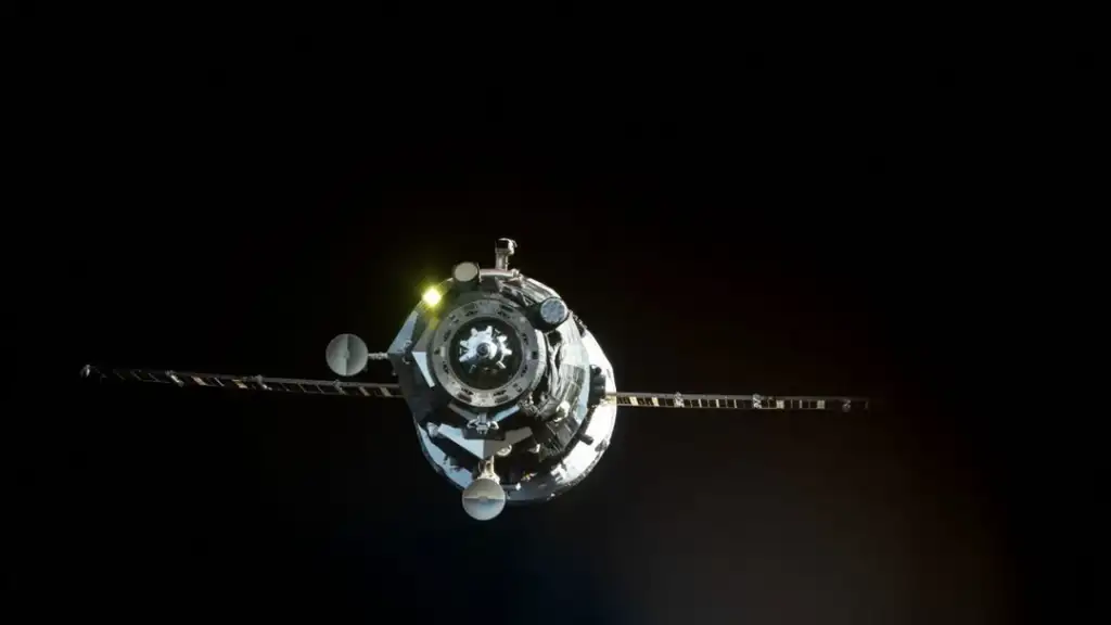 A spacecraft with solar panels extended on both sides is seen against the blackness of space. It is illuminated by reflected sunlight, highlighting its metallic surface and antennae.