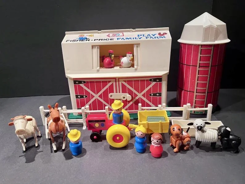 A vintage Fisher-Price Family Farm playset featuring a barn, silo, tractor, animals, and figures. The barn has red and white details, and animals include horses, cows, and dogs. Two figurines wear yellow hats, surrounded by other characters.