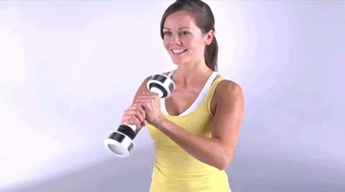 A woman in a yellow tank top smiles while holding a slender handheld exercise device in front of her. The background is a neutral light gray.