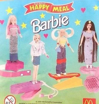 Image of a McDonald's Happy Meal promotional display featuring four Barbie dolls, each with different outfits and accessories. The Barbie logo is prominently displayed above the dolls.