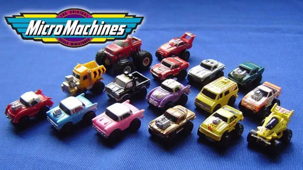 Toy cars from the Micro Machines brand are displayed in rows on a blue background. The cars are in various colors and styles, including trucks and sports cars, with the "Micro Machines" logo in the top left corner.