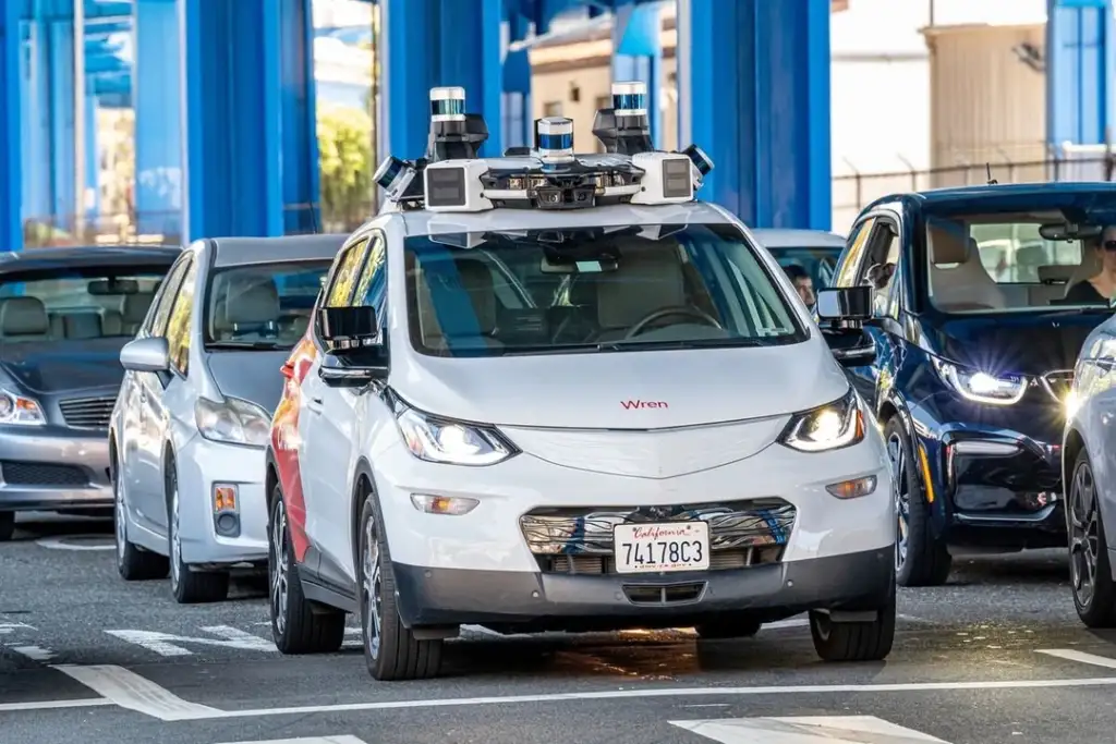 A white self-driving car equipped with sensors and cameras is stopped in traffic on a city street, surrounded by other vehicles. The car has a red and white design, with "Wren" labeled on the front. Prompt text appears to be license plate related.