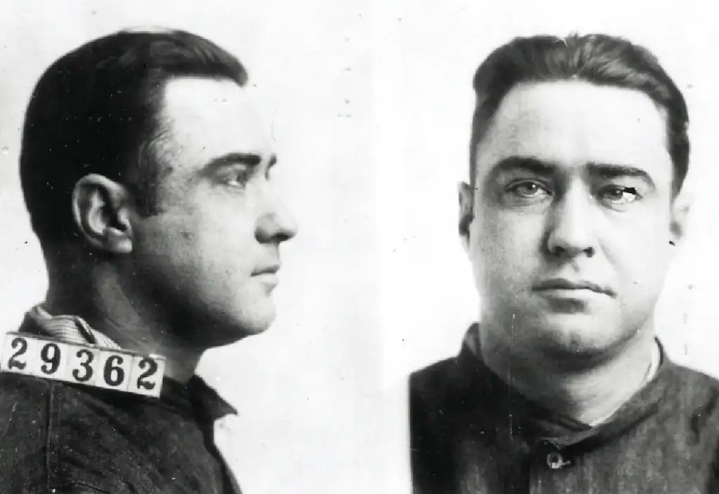 Mugshot of a man with short dark hair, wearing a dark shirt. Two views are shown: profile and front-facing. The number 29362 is visible on a tag by his collar.