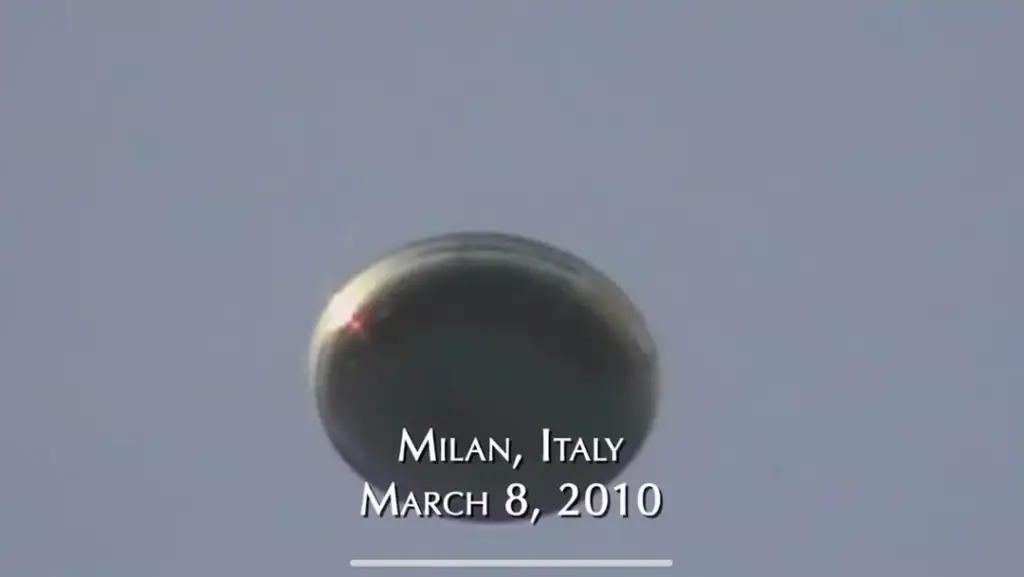 A photo of a metallic, dome-shaped object hovering in the sky against a clear blue background. The text at the bottom reads "Milan, Italy March 8, 2010.