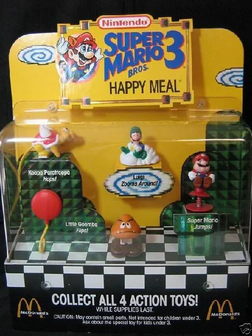 A McDonald's Super Mario Bros. 3 Happy Meal display featuring four plastic action toys: Koopa Paratroopa, Luigi on a cloud, Little Goomba, and Super Mario, each positioned on a checkered platform.