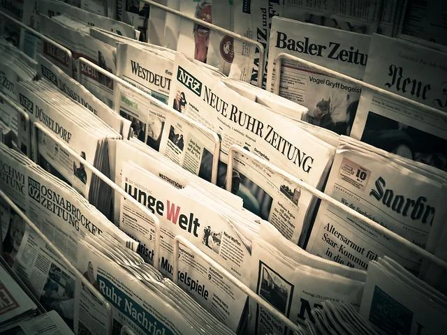 A variety of newspapers are displayed on racks, showcasing different German-language publications. The newspapers are stacked neatly, showing their titles prominently. Some titles include "Basler Zeitung" and "Junge Welt.