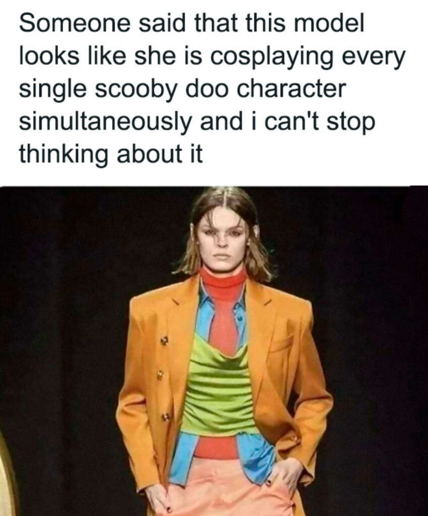 A model walks the runway in an eclectic outfit featuring an orange blazer, green shirt, blue scarf, and coral pants. The text above humorously suggests the model resembles all Scooby-Doo characters at once.