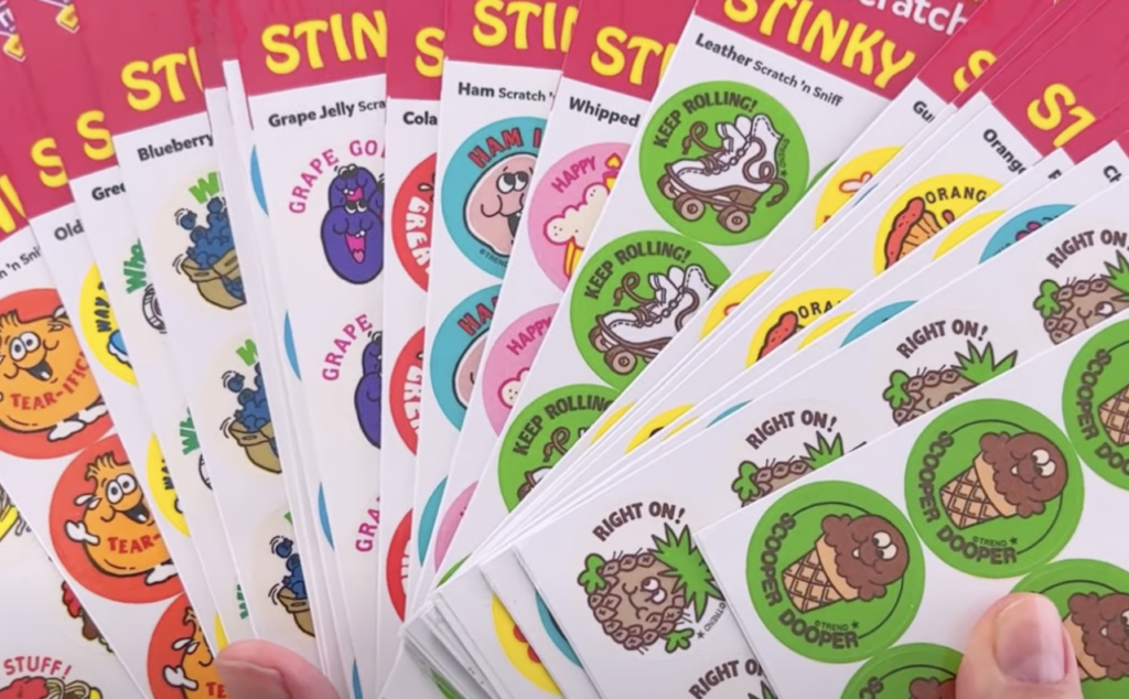 A collection of colorful scratch-and-sniff stickers featuring various cartoon illustrations and phrases like "Keep Rolling" and "Right On!" Each sticker has a different scent, including blueberries, ham, cola, and more.