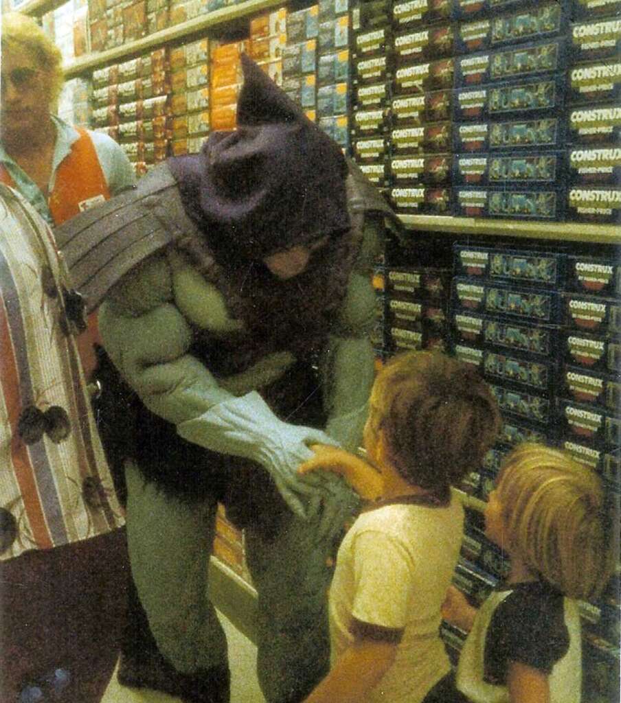 A person in a Skeletor costume interacts with two children in a toy store aisle filled with Construx boxes. Another adult stands nearby, watching the interaction. The children appear curious and engaged.