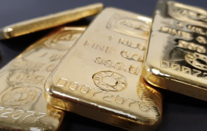 Close-up of several shiny gold bars on a dark surface. The bars are engraved with fine details, including numbers, a stamp, and the word "GOLD." The focus is on the front bar, while others are slightly blurred in the background.