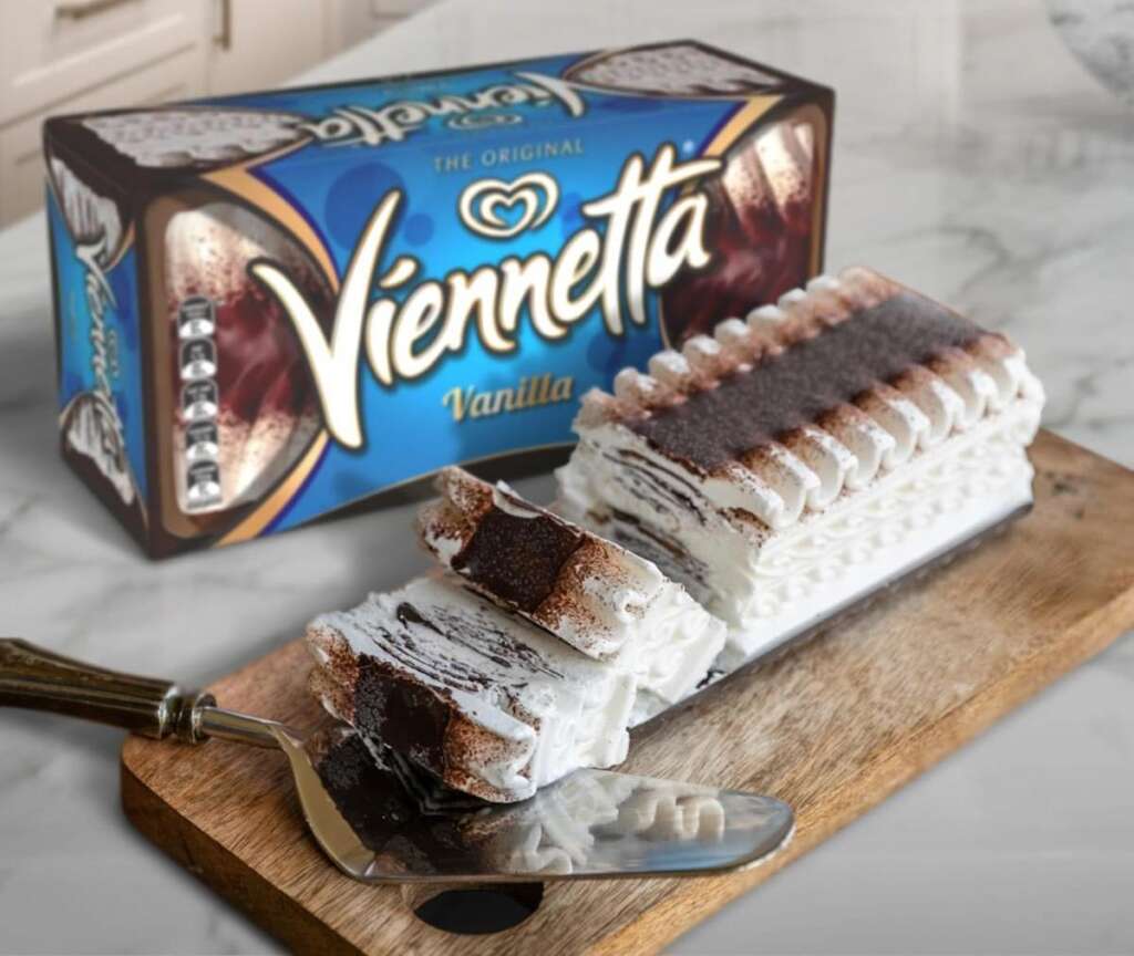 A sliced Viennetta vanilla ice cream cake on a wooden board with a metal serving utensil. The cake has layers of ice cream and chocolate. The box with "Viennetta Vanilla" text is visible in the background.