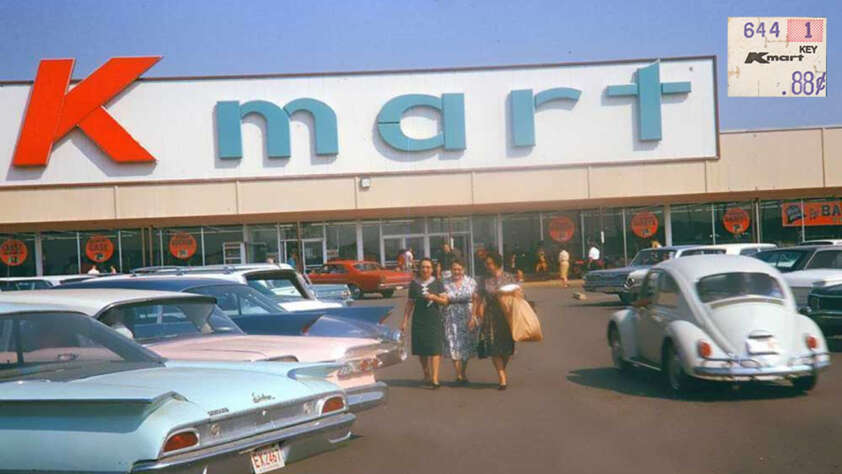 A vintage scene of a Kmart store with a large "Kmart" sign. Shoppers walk in the parking lot among classic cars, including a Volkswagen Beetle. A price tag in the corner shows 88 cents in retro styling.