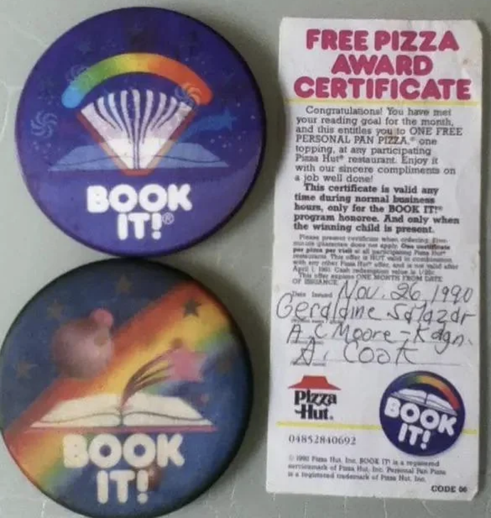 Two round "BOOK IT!" buttons with book and rainbow designs. Nearby, an award certificate for a free personal pan pizza from Pizza Hut, dated November 26, 1990, with handwritten names and details.