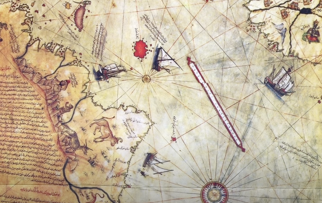 An ancient nautical map featuring an intricately drawn coastline, ships with sails, and compass roses. Handwritten inscriptions and illustrations of sea creatures and land animals are visible on the aged parchment.