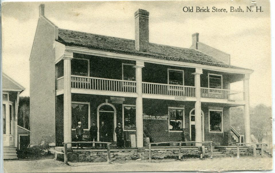 Vintage black and white photo of the Old Brick Store in Bath, New Hampshire. Features a two-story building with a porch, four people standing in front, and signage reading "Groceries" and "Dry Goods & Notions.