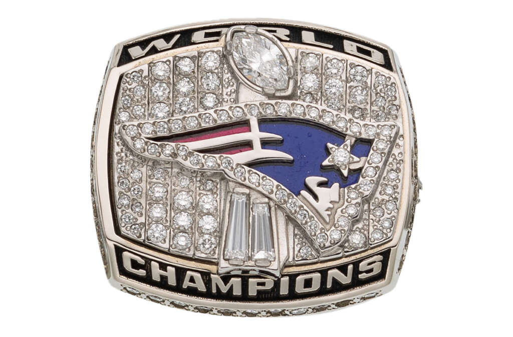 A ring featuring the design of a flying emblem with stars and stripes, surrounded by numerous small jewels. The words "World Champions" are engraved around the edges. The ring has a luxurious and ornate appearance.