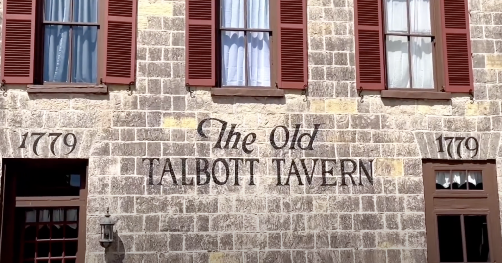 Stone building facade of The Old Talbott Tavern, dated 1779, featuring large windows with red shutters and white curtains. The words "The Old Talbott Tavern" are prominently displayed on the wall.