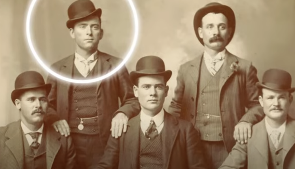 Sepia-toned vintage photo of five men posing in suits and bowler hats. One man is highlighted with a circular glow around his head, standing out from the rest. They appear to be from the late 19th or early 20th century.