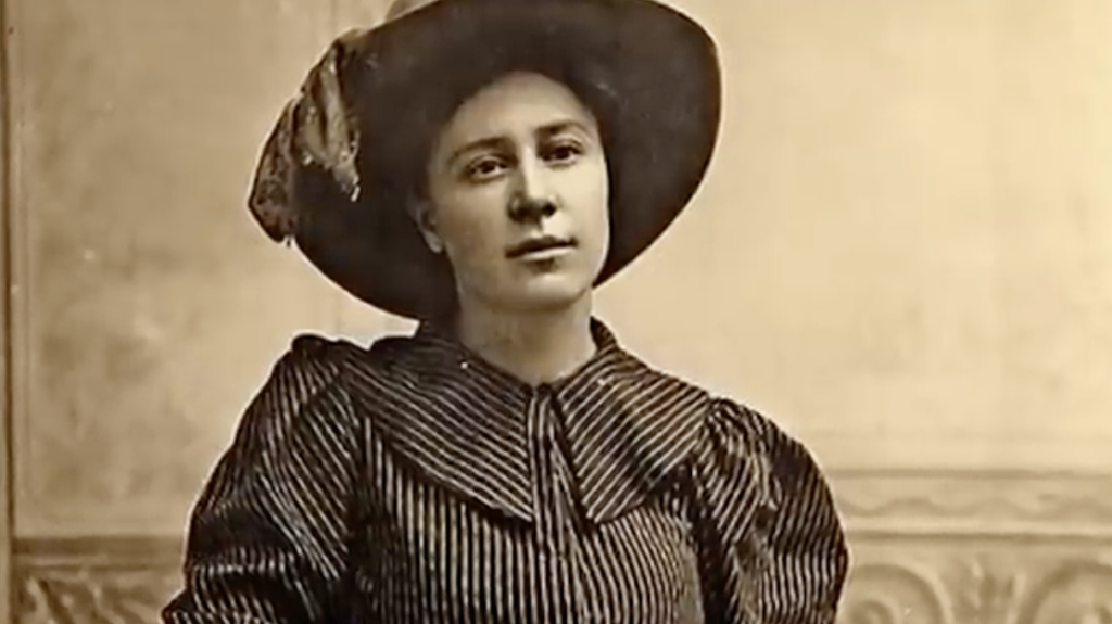 Vintage sepia-toned portrait of a young woman wearing a wide-brimmed hat and a striped, puff-sleeved dress. She looks slightly to the side with a calm expression, set against a simple backdrop with subtle details.