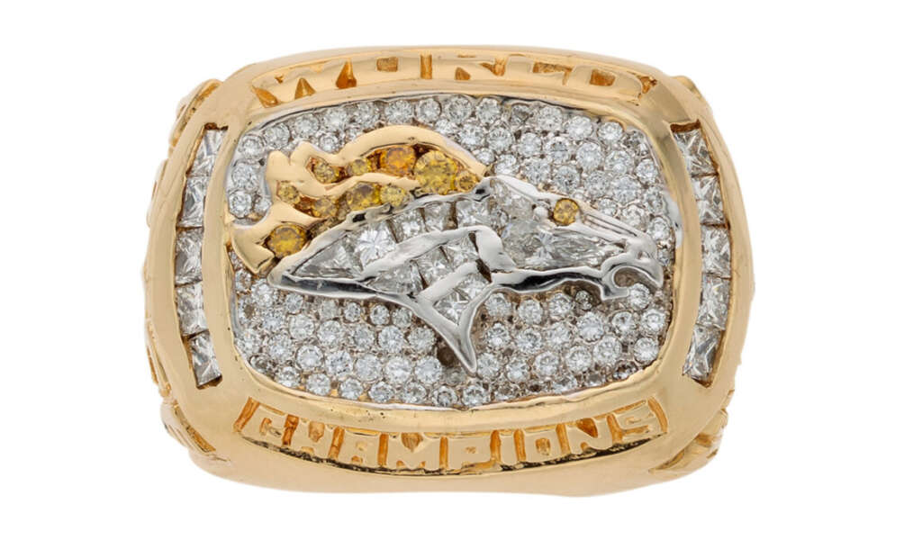 A gold championship ring adorned with numerous diamonds and featuring the image of a horse head. The words "World Champions" are engraved around the central emblem.