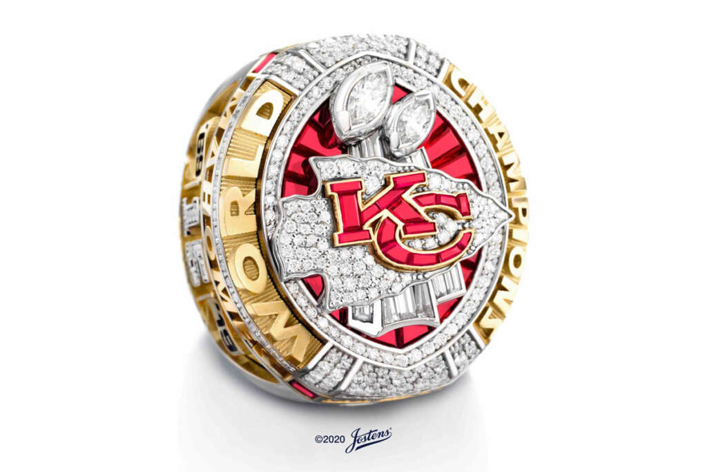 A gold and silver ring with the Kansas City Chiefs logo surrounded by diamonds. The words "World Champions" are inscribed around the edge. Two Lombardi Trophies are depicted above the logo. The ring is designed by Jostens, marked with 2020.