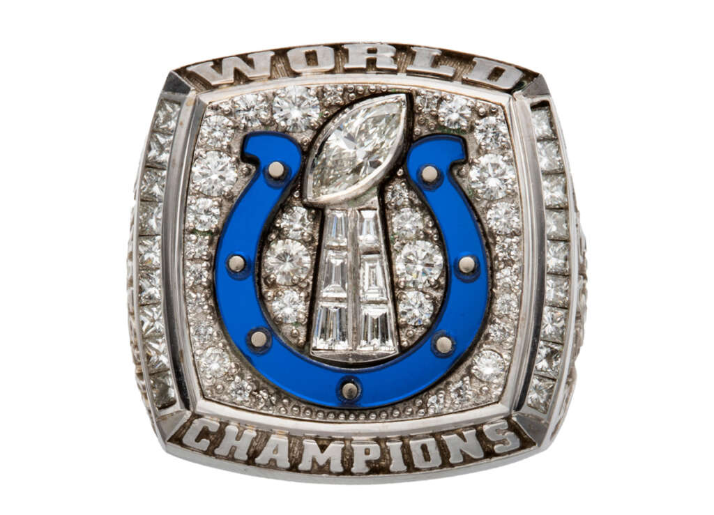 Championship ring featuring a silver and blue horseshoe emblem, encrusted with diamonds surrounding a Lombardi Trophy design. It reads "WORLD CHAMPIONS" on the top and bottom, with additional diamonds set along the borders.