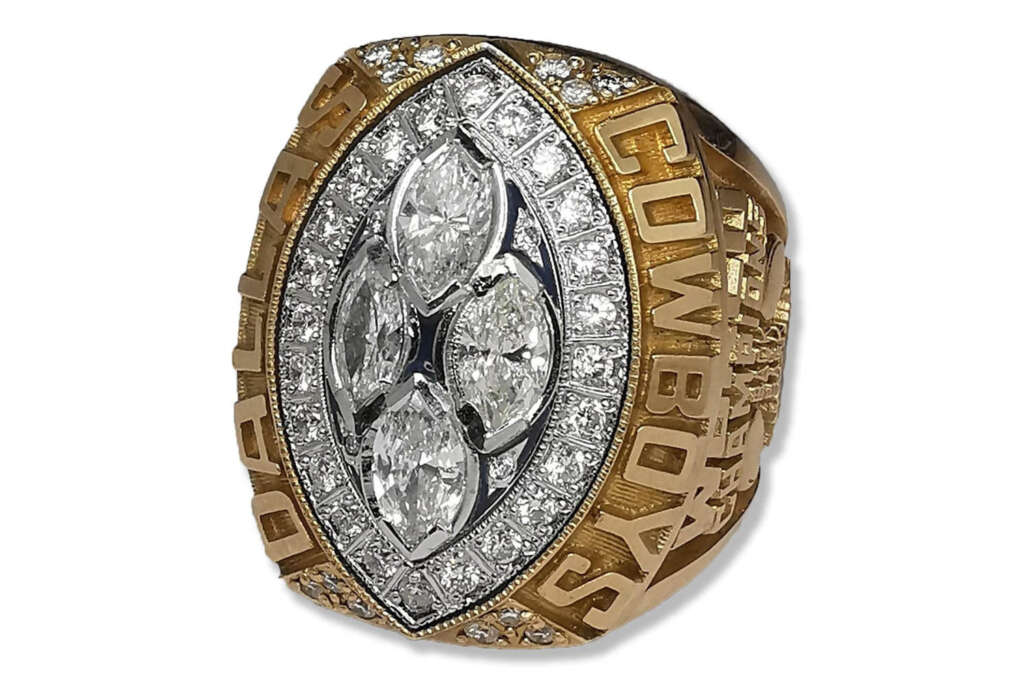 A gold and silver championship ring featuring a cluster of large, marquise-cut diamonds surrounded by smaller round diamonds. The words "Dallas Cowboys" are engraved around the edges.