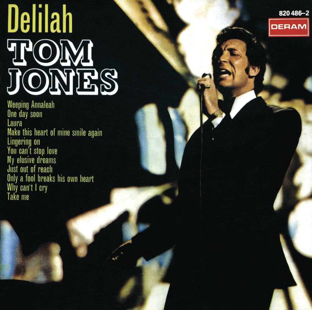 A man in a suit holding a microphone sings on stage. The album cover features "Delilah" and "Tom Jones" prominently. A list of song titles is displayed on the left. A logo "Deram" is in the top right corner.