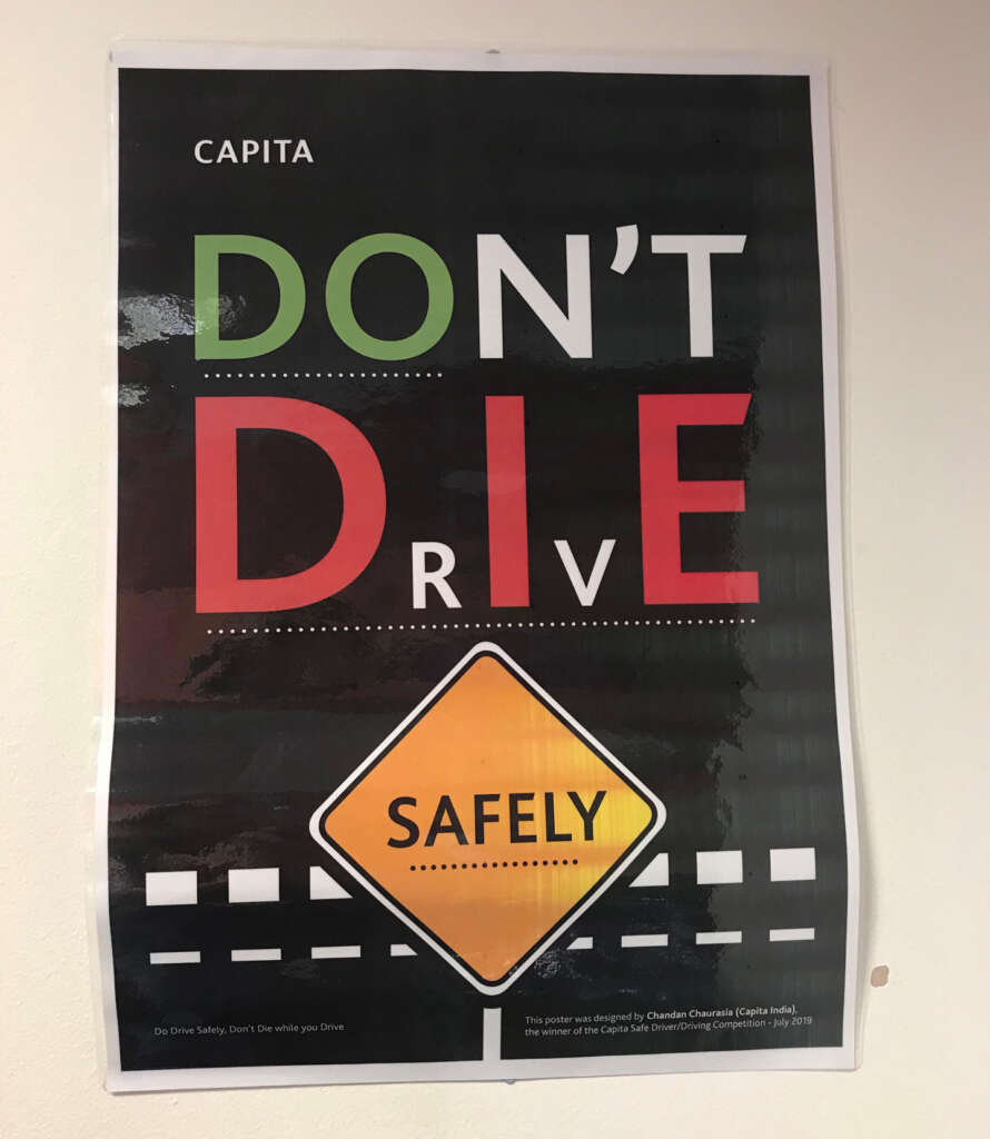 A poster with the words "DON'T DRIVE" in large letters and "SAFELY" inside a yellow road sign shape below. The poster features a road-like background with white dashed lines and includes the message: "Do Drive Safely. Don't Drink While You Drive.