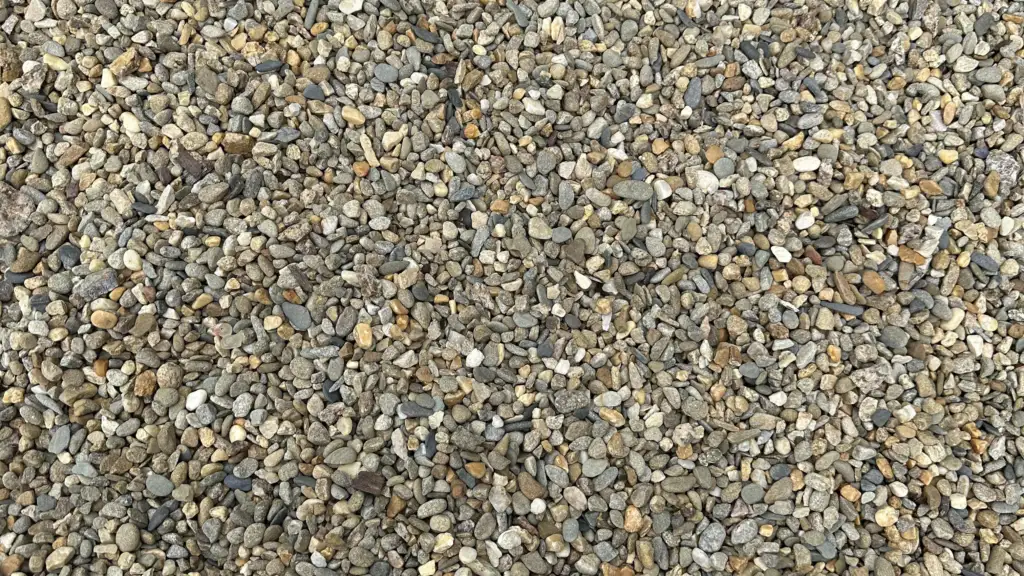 A close-up view of a large collection of small, multicolored pebbles. The stones vary in shades of gray, brown, and beige, creating a textured surface.