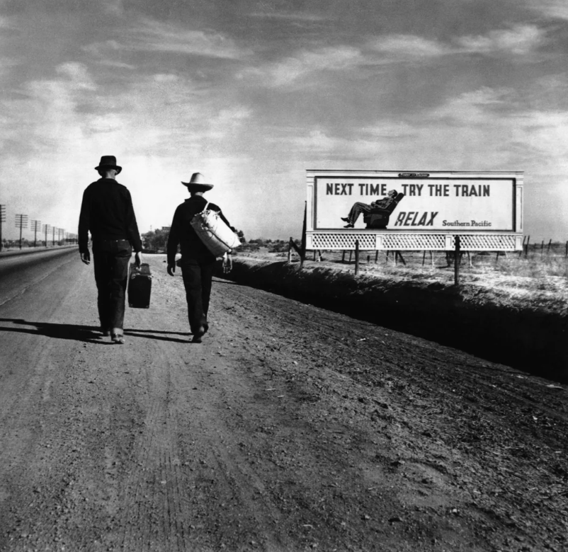 Two men in hats walk along a deserted road carrying belongings. A billboard on the right reads, "Next time... try the train. Relax. Southern Pacific." The sky is cloudy, and the landscape is flat and open.