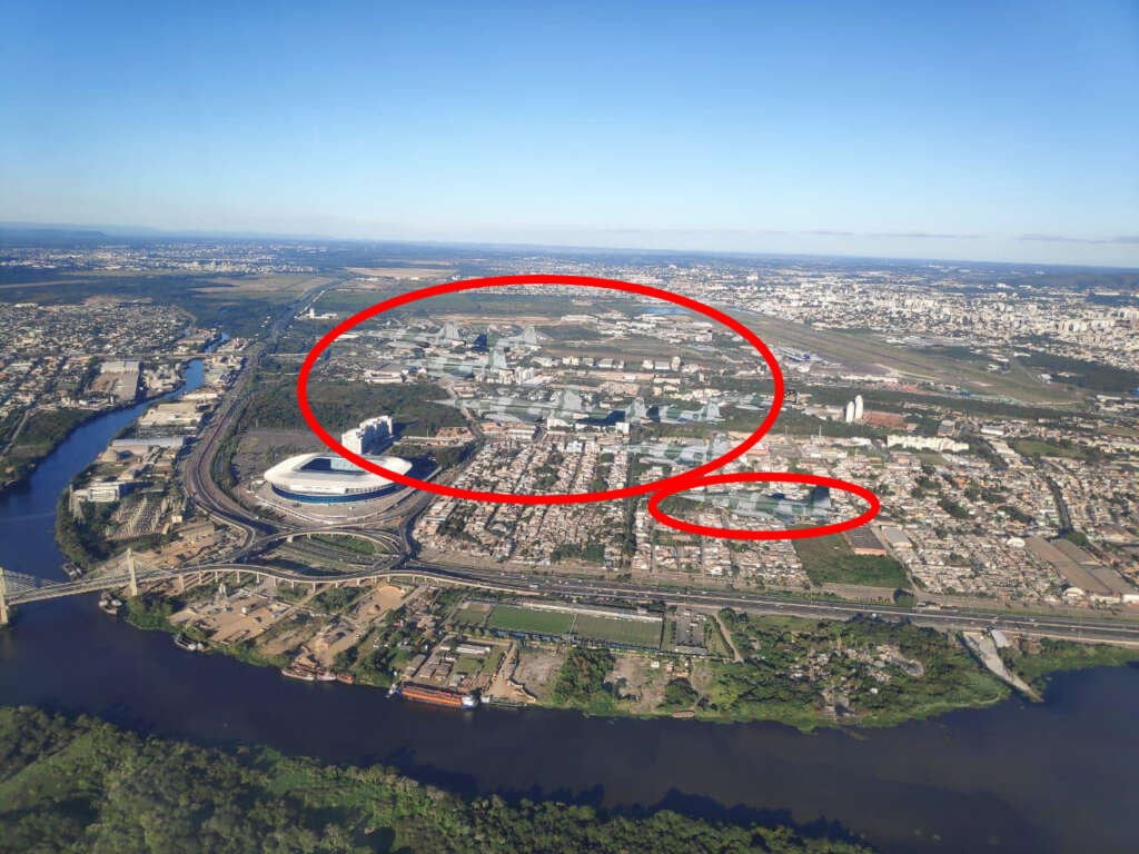 Aerial view of a cityscape with a river running through it. Two large red circles highlight areas within the city. Buildings, roads, and green spaces are visible under a clear blue sky.