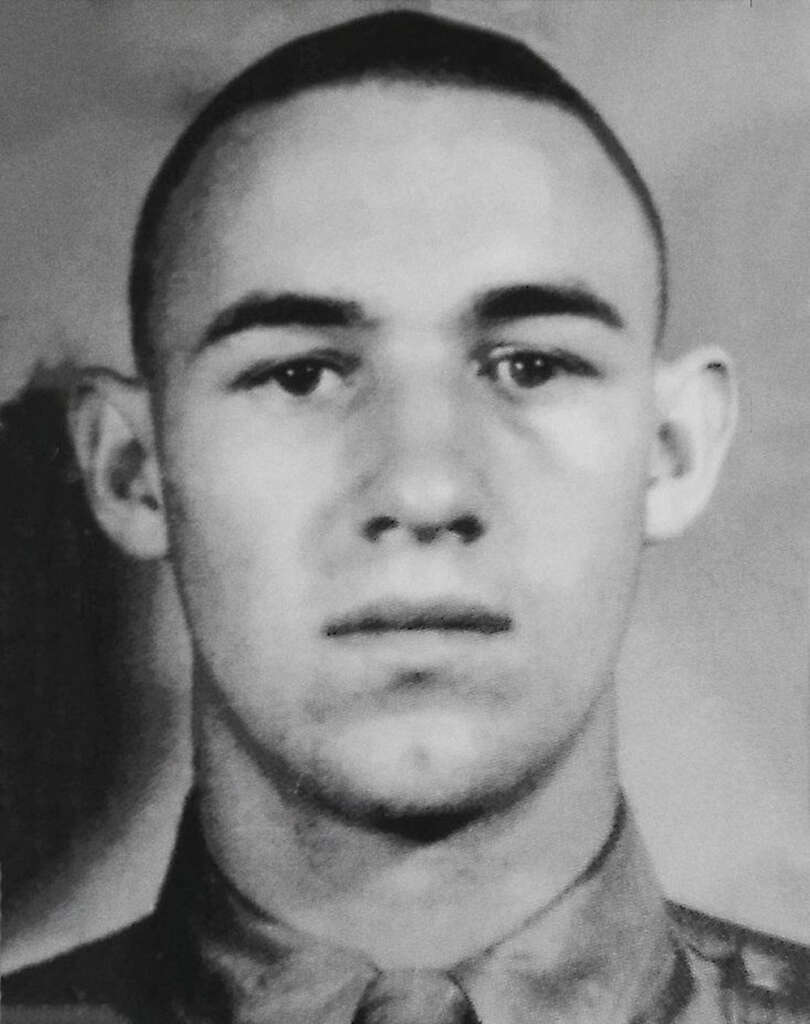 Black and white portrait of a young man with short hair, wearing a collared shirt. The background is plain and the expression is neutral.