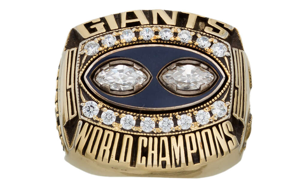 A gold championship ring featuring the word "GIANTS" on the top, surrounded by diamonds. Below are the words "WORLD CHAMPIONS." Two large diamond-shaped gems are in the center, encircled by smaller diamonds.