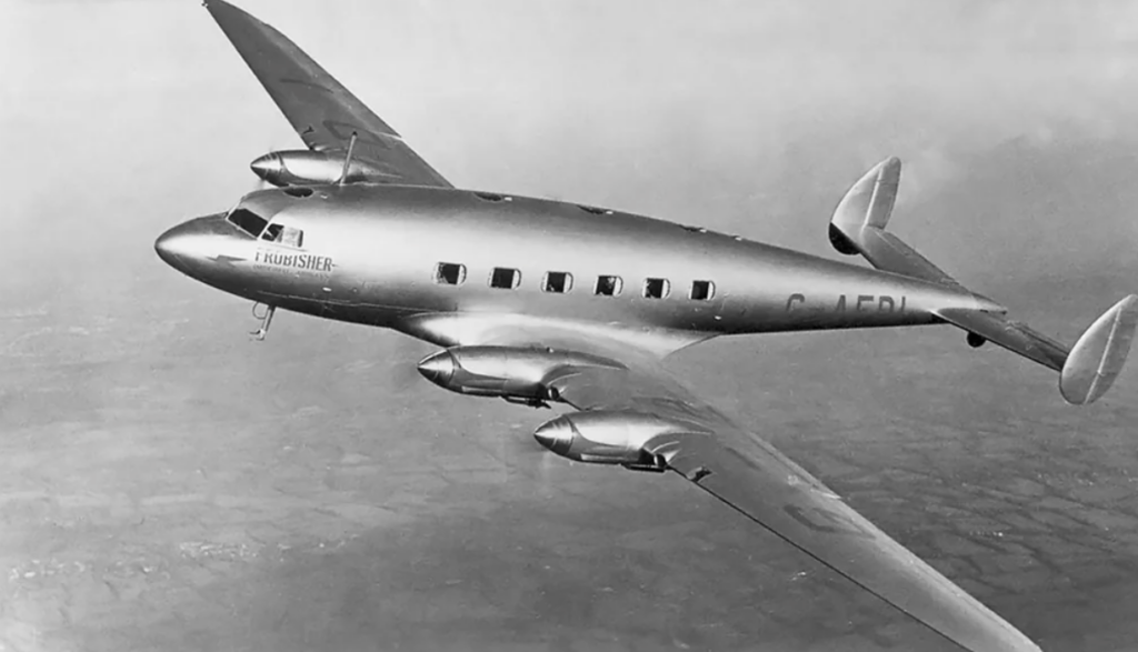 A vintage silver aircraft with four engines, labeled "G-AERL" and "FROBISHER," is flying over a landscape. The plane has a streamlined design with multiple windows along the side and distinctive tail fins.