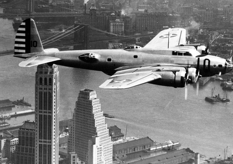 A vintage B-17 bomber aircraft flies above a cityscape, showcasing skyscrapers and bridges. The city below appears busy, with buildings and waterways visible. The plane's American military markings are prominent.