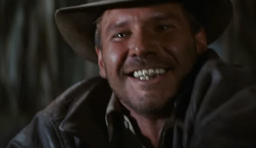 A person wearing a cowboy hat and leather jacket smiles with an adventurous expression. The background is blurred, suggesting movement or excitement.