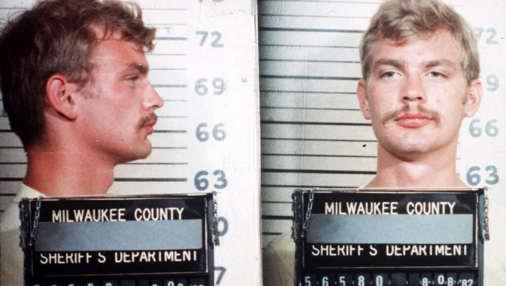 A mugshot shows a man with light hair and a mustache, facing left in the profile view and forward in the front view. He is holding a board with text indicating Milwaukee County Sheriff's Department. Lines in the background indicate height.