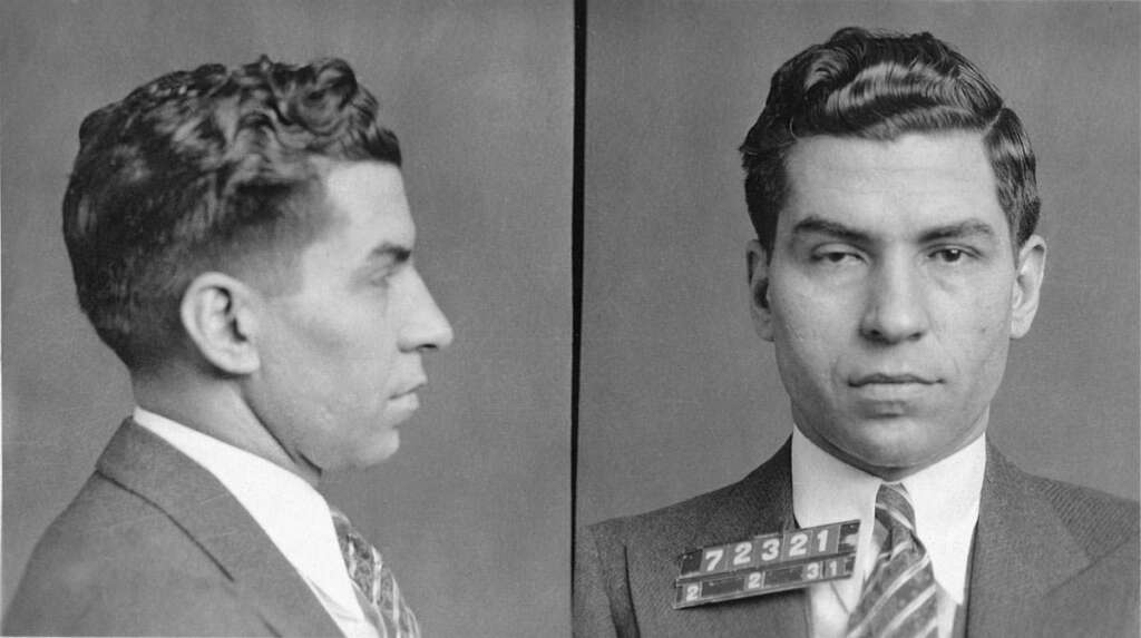 Black and white mugshot of a man in a suit and tie. He has short, wavy hair and appears in a front and side profile. A small plaque with numbers is on his chest.