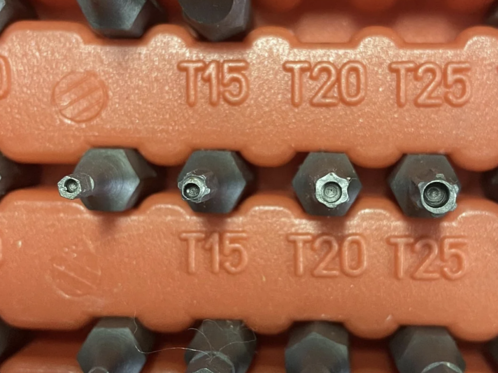 Close-up of a set of hexagonal screwdriver bits in a red plastic holder, labeled with sizes T15, T20, and T25. The bits are metallic and arranged vertically in rows, each corresponding to its labeled size.