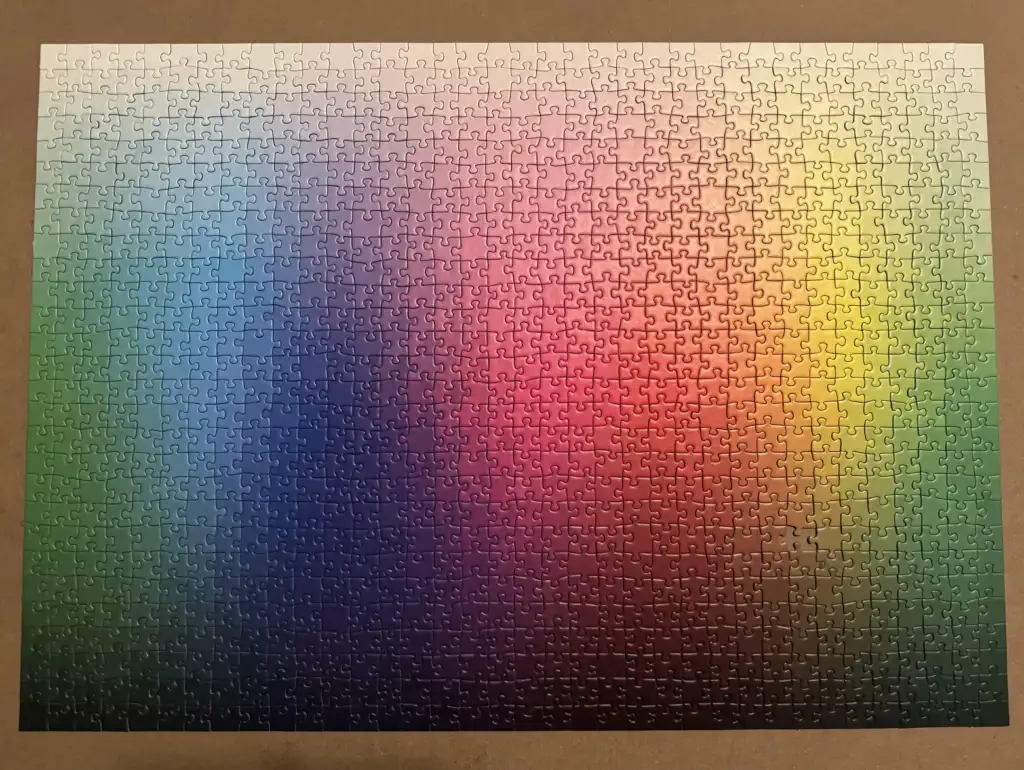 A completed jigsaw puzzle displays a gradient of colors, transitioning smoothly from white at the top to dark shades at the bottom, with a rainbow spectrum of blue, green, red, and yellow in the center.