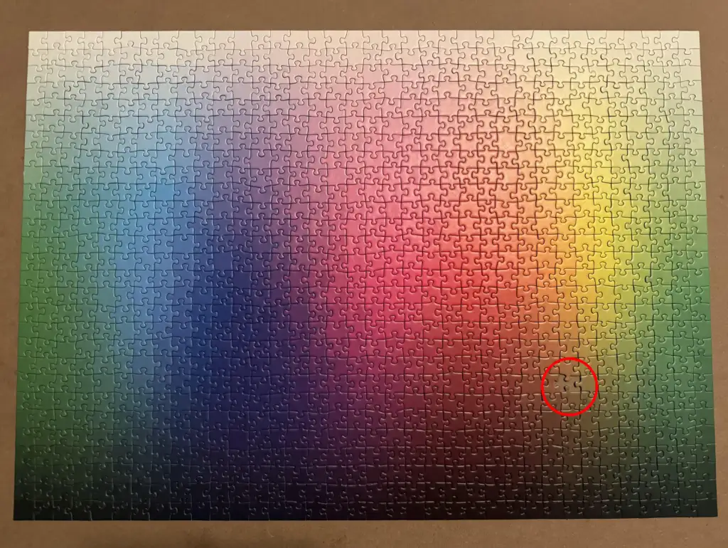 A gradient jigsaw puzzle completed, displaying a smooth transition from cool colors like blues and greens on the left to warm colors such as reds and yellows on the right. A red circle highlights a piece in the lower right quadrant.