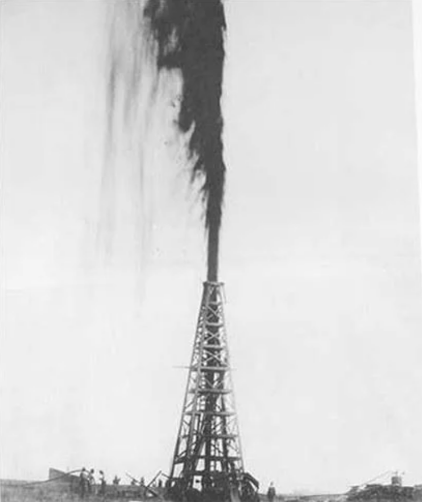 Black and white historical photo of an oil derrick gushing oil high into the air. Workers surround the base, and the structure is set against a clear sky, highlighting the dramatic height of the oil spray.